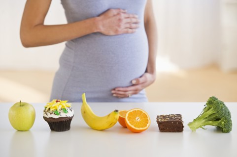 Pregnant woman standing behind a row of food.