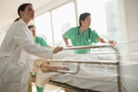 Healthcare workers pushing gurney in emergency room.