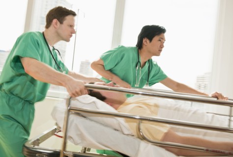 Healthcare workers pushing gurney in emergency room.