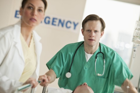 Healthcare workers pushing gurney in emergency room.