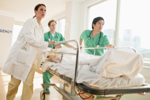 Healthcare workers pushing gurney in emergency room.
