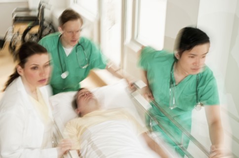 Healthcare workers pushing gurney in emergency room.