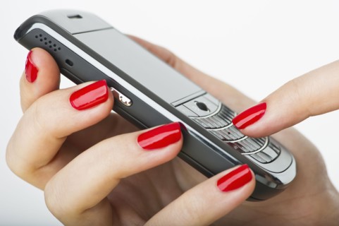 Woman wearing red nail polish texting on cell phone.
