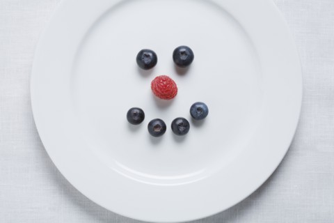 Smiley face of blueberries and raspberry on white plate. Photographe : Kristin Lee