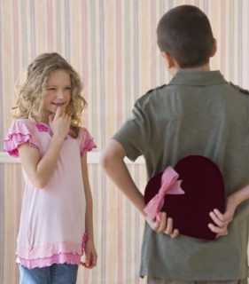 Young boy hiding a box of chocolates from young girl.