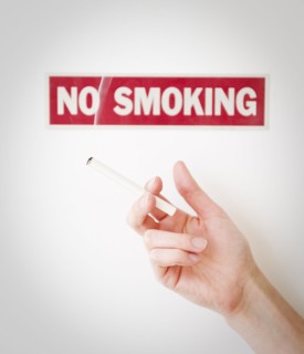 Hand holding cigarette in front of no smoking sign. Photographe : Jamie Grill