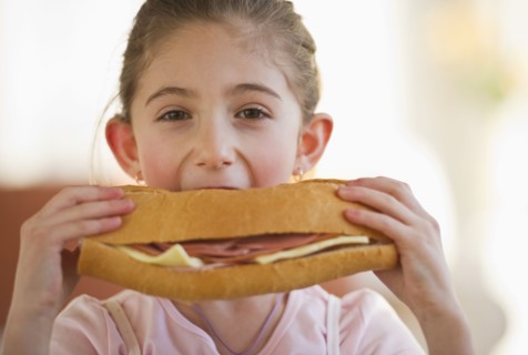 Young girl eating a large sandwich. Photographe : Daniel Grill