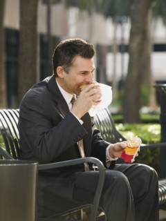 Businessman eating lunch on park bench.
