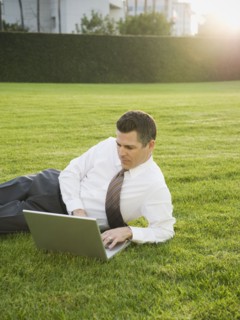 Businessman relaxing with laptop on lawn.