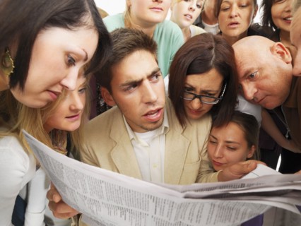 Group of people reading one newspaper. Photographe : momentimages