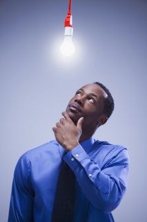 Contemplative businessman standing under a light bulb. Photographe : Mike Kemp