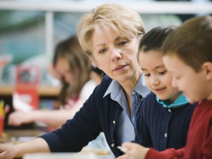 Teacher sitting at table with kindergarten students.