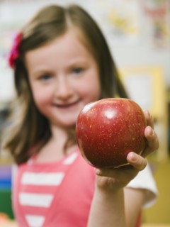 Kindergarten student holding an apple in classroom.