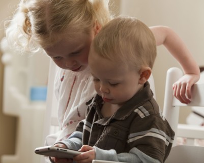 Young siblings looking at cell phone together. Photo : Mike Kemp