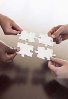 Four hands holding puzzle pieces.