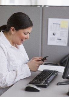 Businesswoman texting at her desk in cubicle.