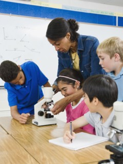 Teacher helping students use microscope in science lab.
