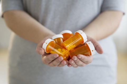 Hands holding several bottles of prescription medication.