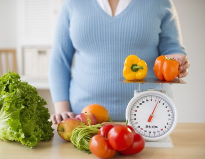 Overweight woman measuring peppers on a food scale.