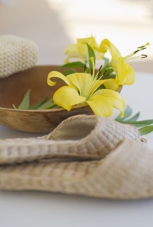Slippers beside a wooden bowl with yellow lilies in it.