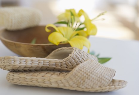 Slippers beside a wooden bowl with yellow lilies in it.