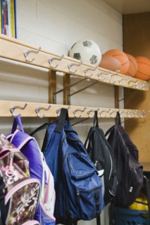 Children's backpacks hanging on hooks in classroom.