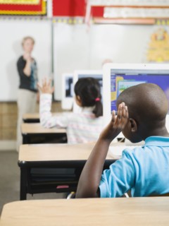 Elementary school students raising their hands in classroom.
