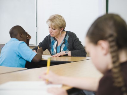 Teacher helping student in elementary school classroom.