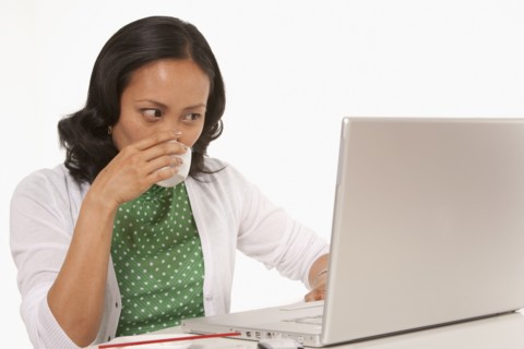 Woman drinking coffee while working on laptop. Photo : K.Hatt