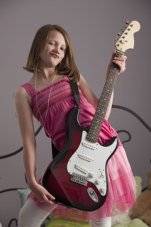 Young girls playing guitar on her bed. Photo : Mike Kemp