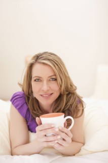 Woman lying down with a cup of coffee. Photo : Dan Bannister