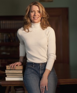 Woman leaning against table beside stack of books. Photo : Dan Bannister