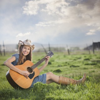 Cowgirl sitting in field playing guitar. Photo : Mike Kemp