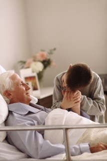Grandfather lying in hospital bed as his grandson holds his hand. Photo : Rob Lewine