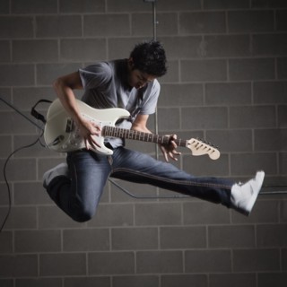 Man jumping in air while playing guitar. Photo : Mike Kemp