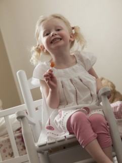 Young girl in rocking chair eating a sucker. Photo : Mike Kemp