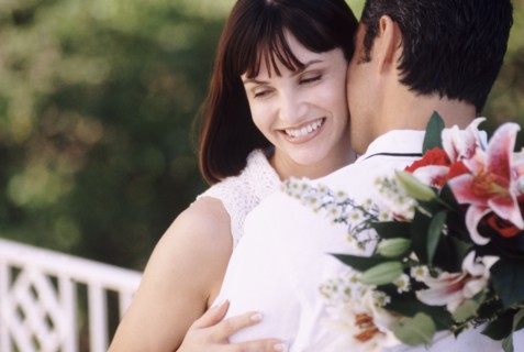 Man kissing woman as he holds flowers behind his back. Photo : Rob Lewine