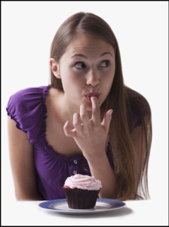 Woman sneaking a lick of icing from a cupcake. Photo : Mike Kemp