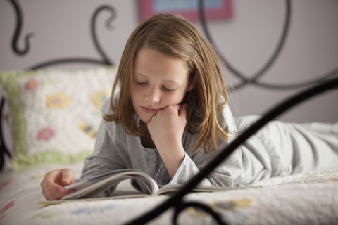Young girl reading on her bed. Photo : Mike Kemp