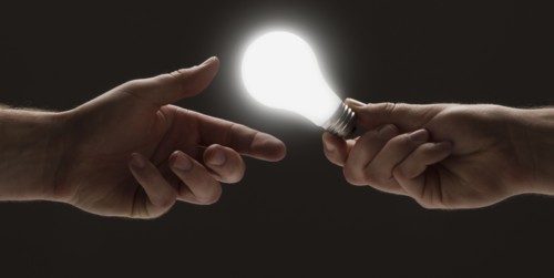 Hand passing a light bulb to another hand. Photo : Mike Kemp