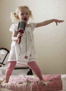 Young girl singing on her bed. Photo : Mike Kemp