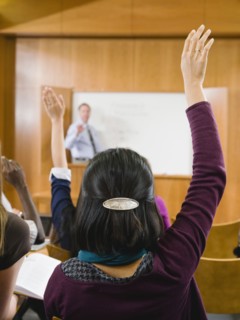 College students raising their hands in lecture hall.