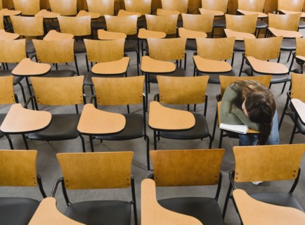College student sleeping in empty lecture hall.