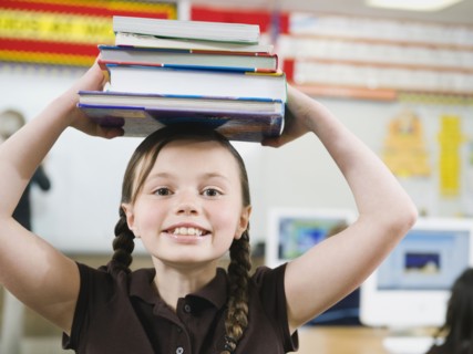 Elementary student holding a stack of books on her head.
