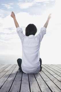 Woman sitting on porch with her arms raised. Photo : momentimages