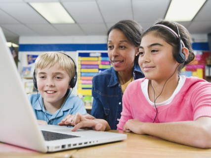 Teacher helping students use laptop.