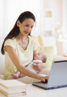 Mother typing while holding baby.