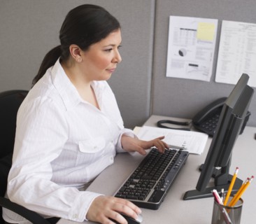 Businesswoman working on laptop in cubicle.