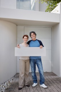 Couple standing in front of their home. Photo : momentimages