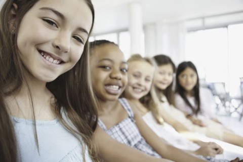 Group of young girls sitting in a row. Photo : momentimages